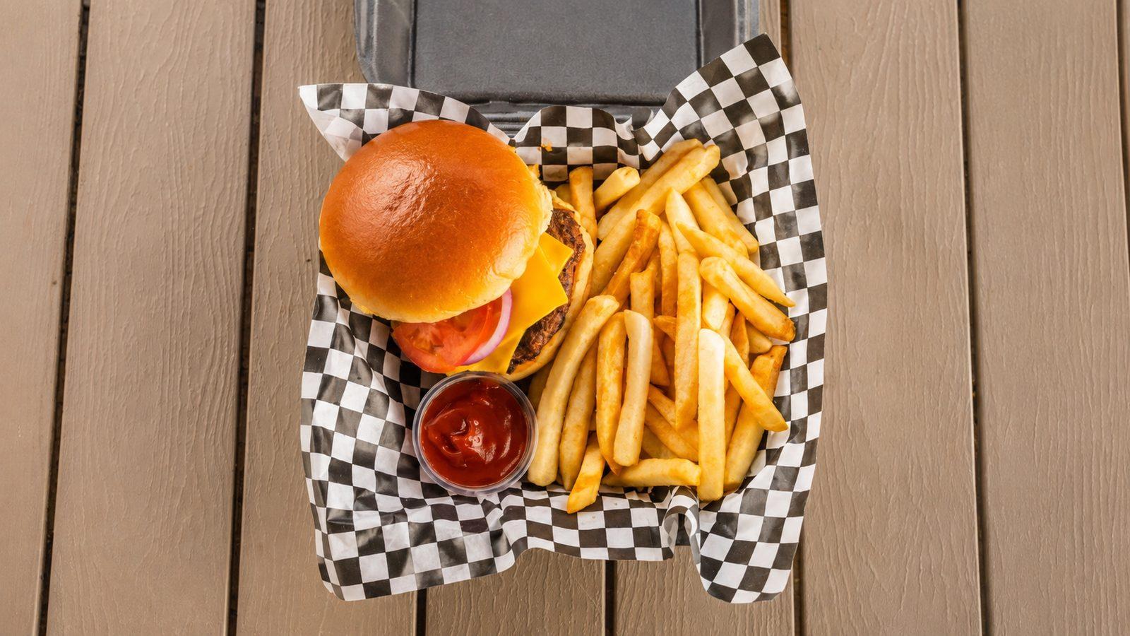Grilled beef burger with fries and ketchup in a checkered-paper basket