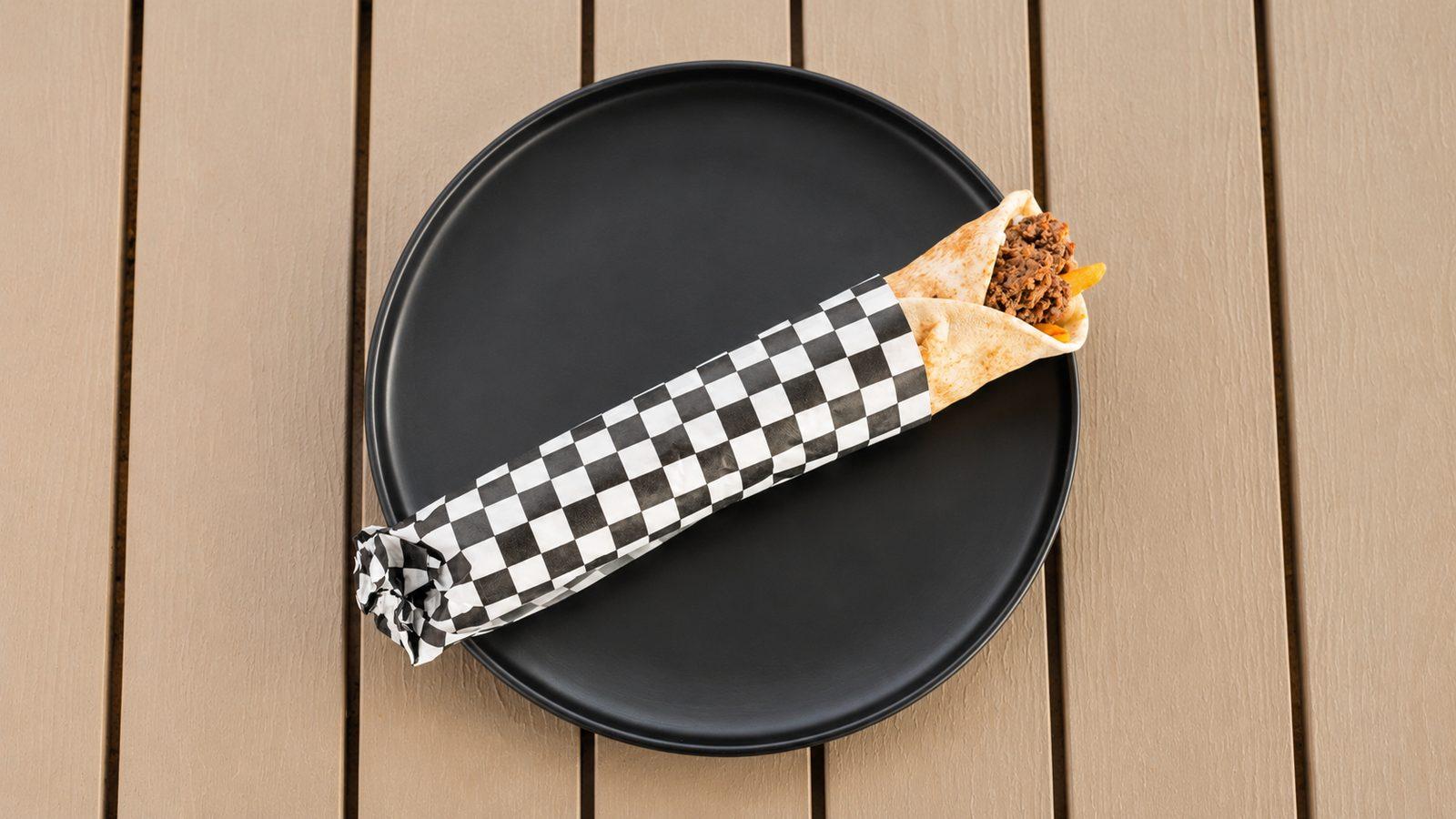 Grilled beef kebab wrap in checkered paper on a black plate
