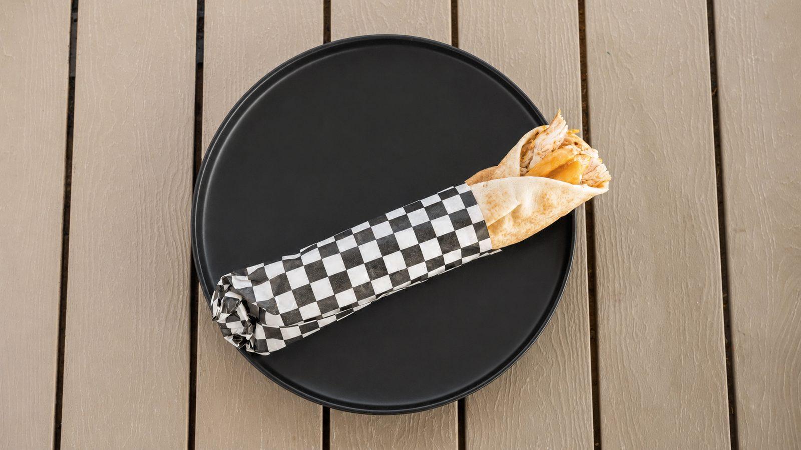 Grilled chicken shawarma wrap in checkered paper on a black plate
