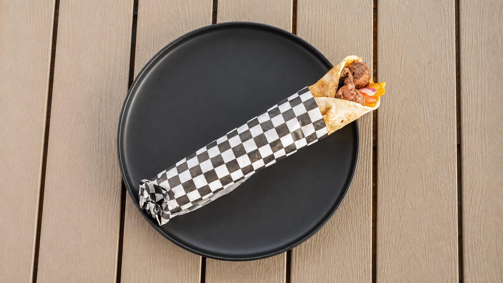 Grilled lamb skewer wrap in checkered paper on a black plate