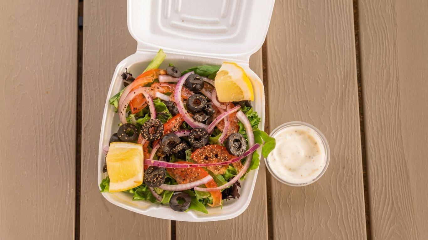House salad with olives, red onion, tomato and lemon in a takeout box